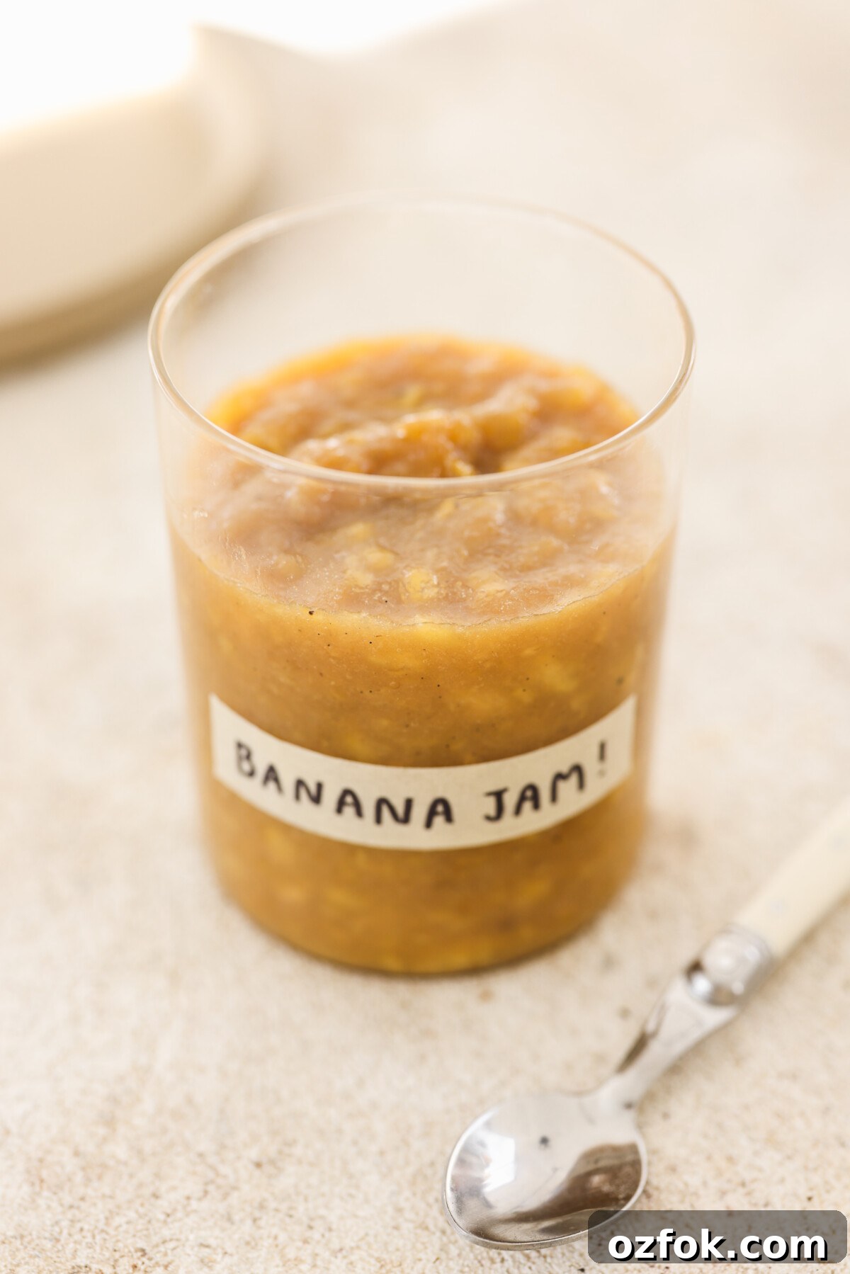 Vegan Homemade Banana Jam Recipe: Simple Step-by-Step Guide 2 a glass jar labeled "banana jam" with a white spoon resting next to it.