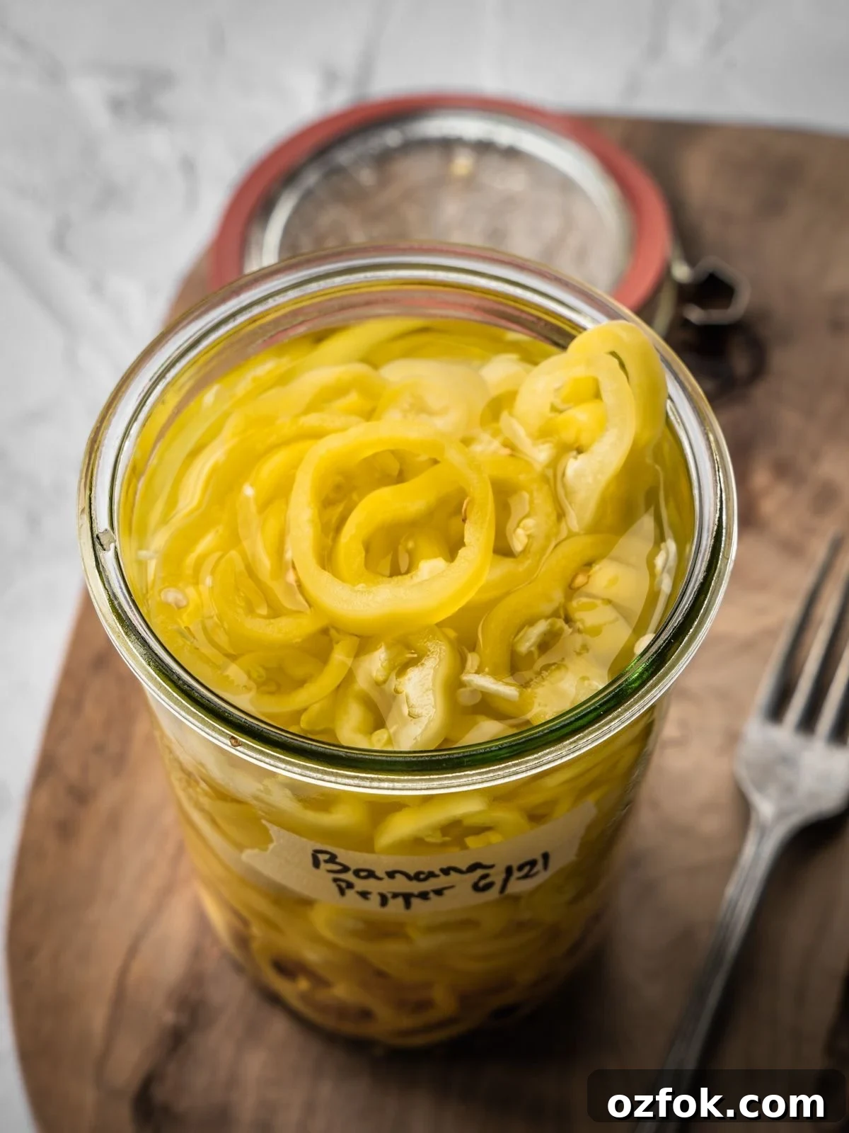An open jar of pickled banana peppers on a wooden board.