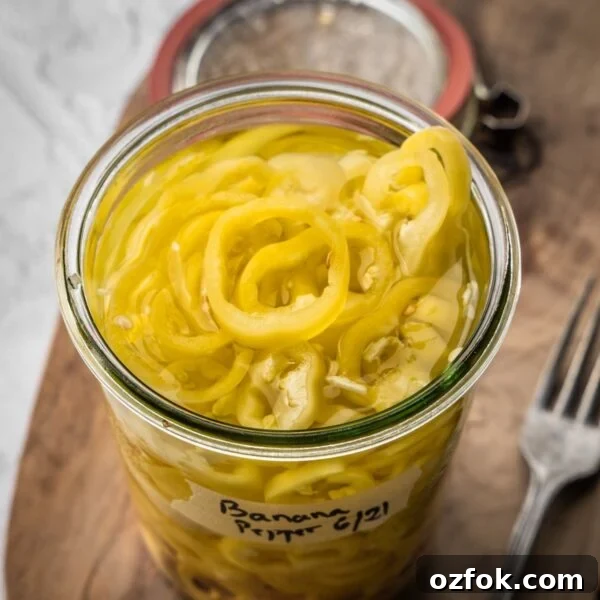 An open jar of pickled banana peppers on a wooden board.