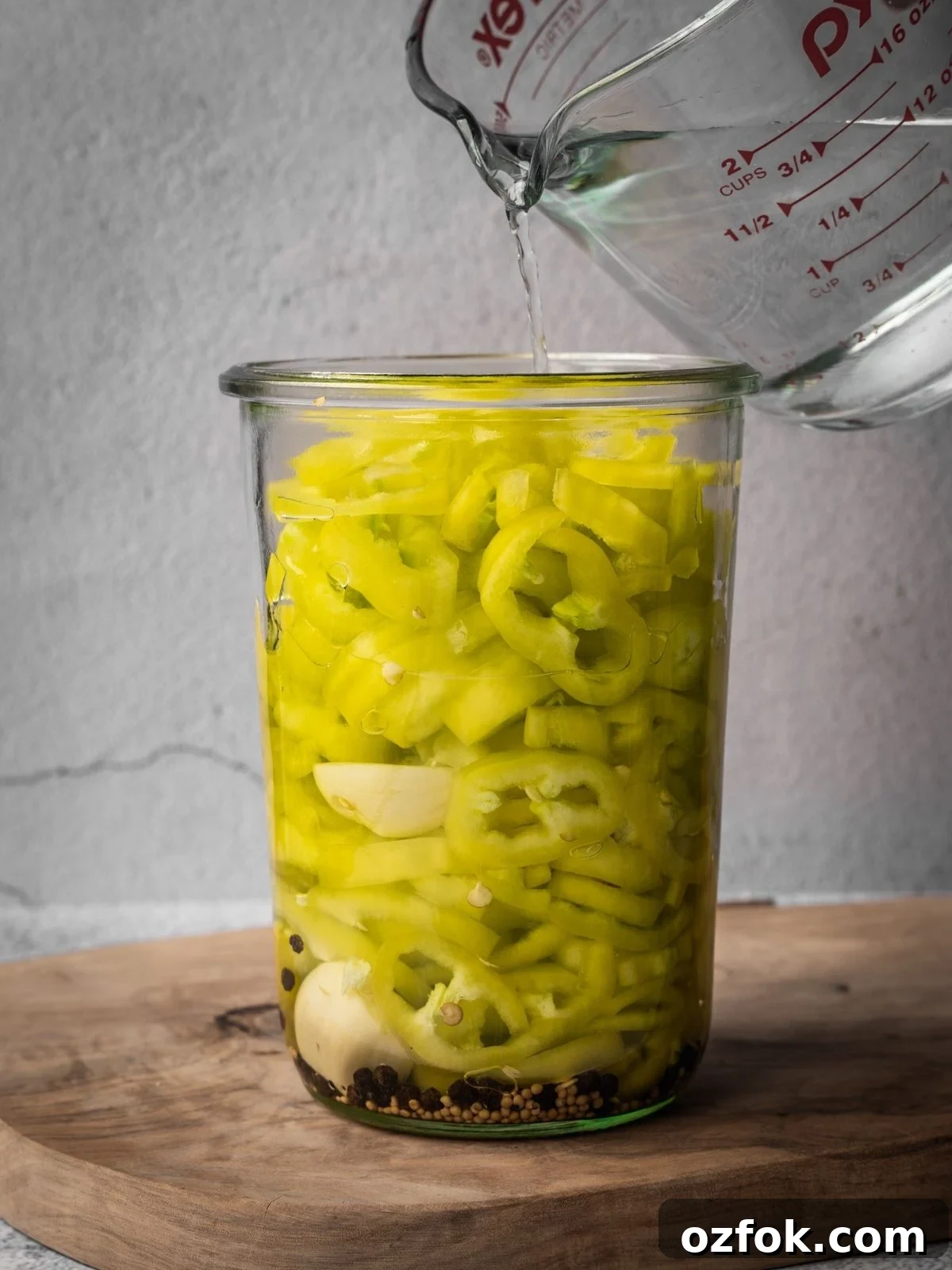 Pouring the pickling solution over the peppers in the mason jar.