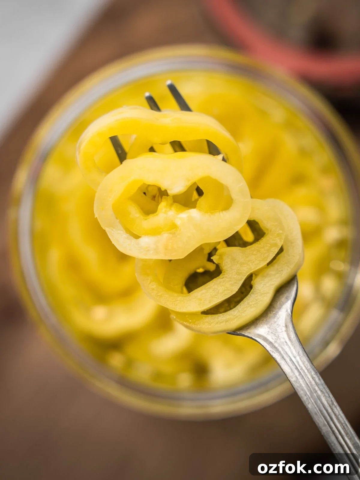 An open jar of pickled banana peppers on a wooden board.