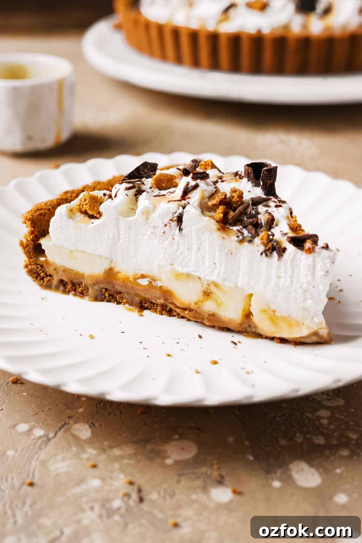 Banoffee Tart Recipe: Caramelized Banana Tart with Buttery Crust 2 A slice of banoffee tart on a plate showing layers of dulce de leche, bananas and whipped cream.