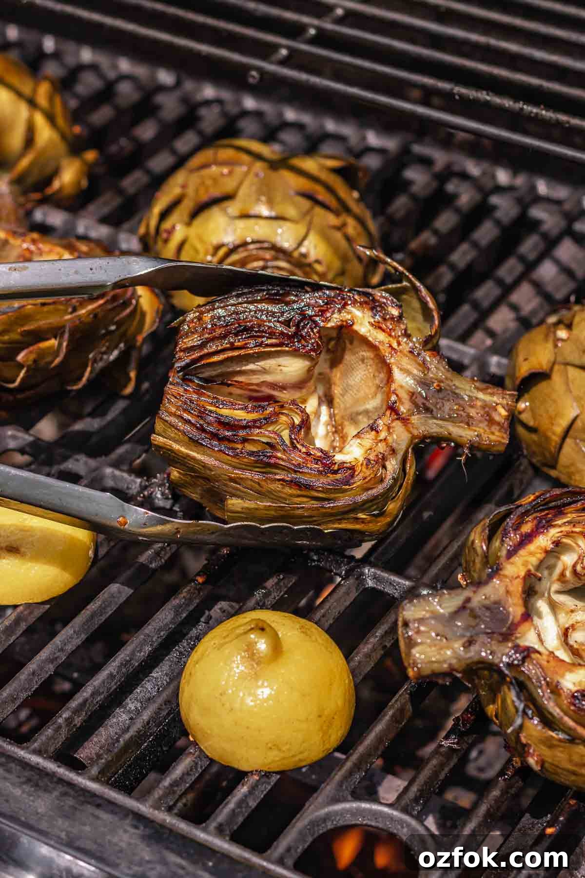 Grilled Marinated Artichokes with Lemon Aioli Recipe 15 Tongs flip a charbroiled artichoke on the grill.