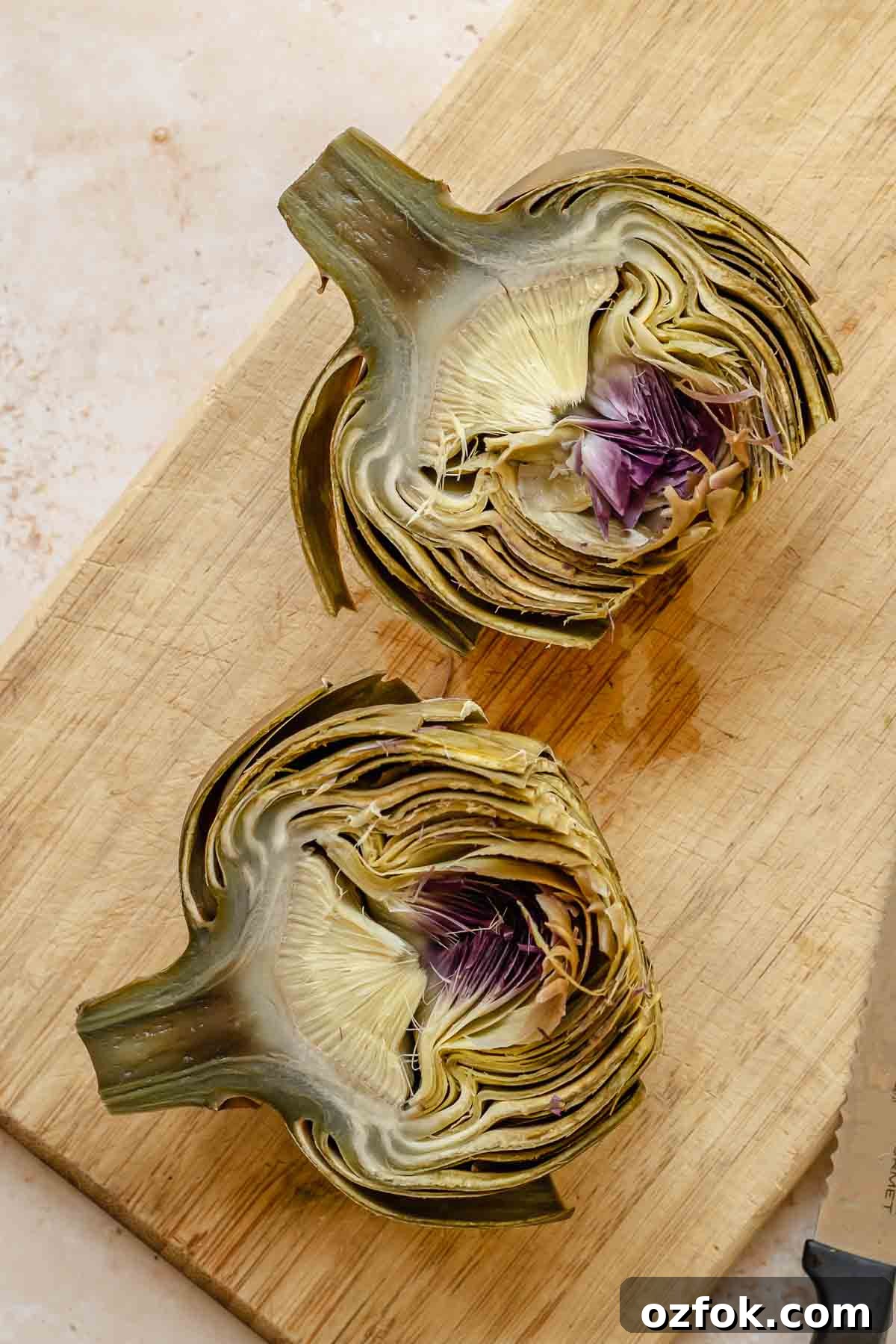 Grilled Marinated Artichokes with Lemon Aioli Recipe 8 Steamed artichokes cut in half on a cutting board.