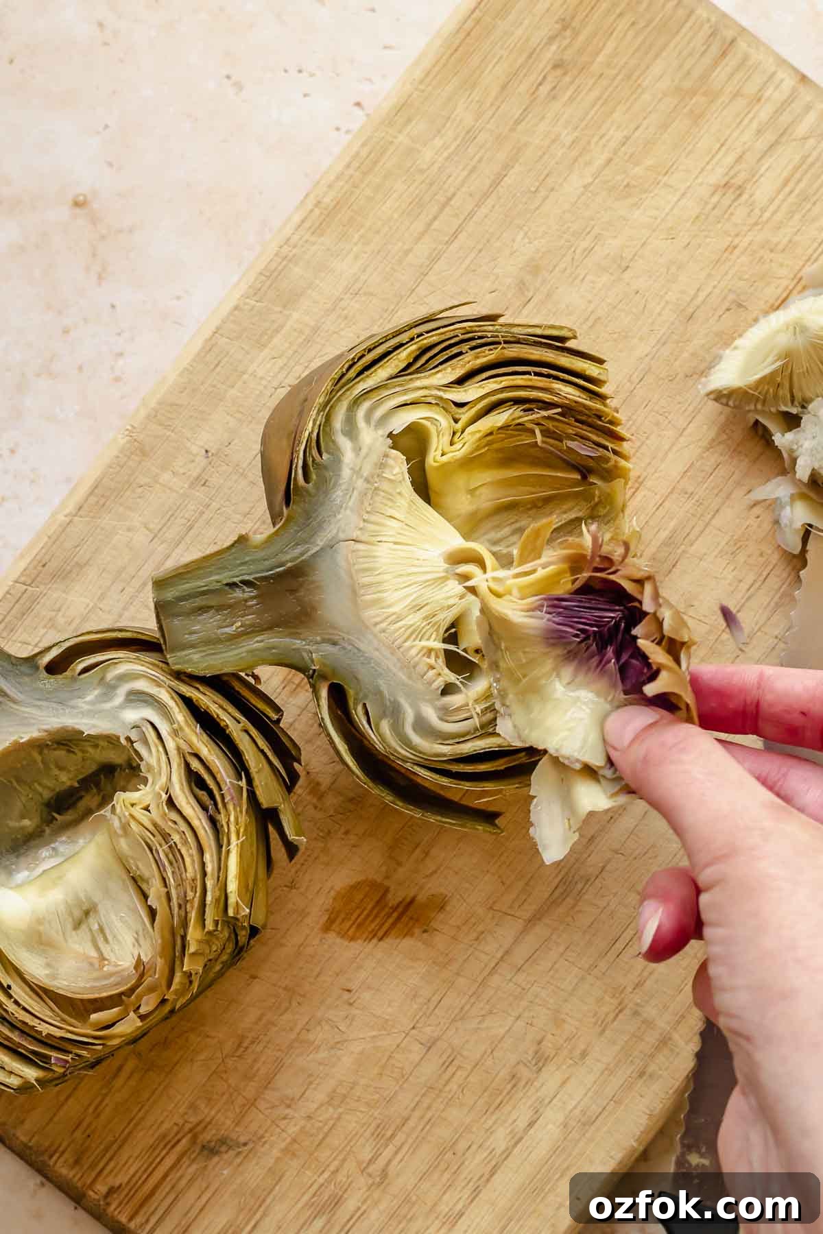 Grilled Marinated Artichokes with Lemon Aioli Recipe 9 A hand removes the purple leaves from the inside of an artichoke.