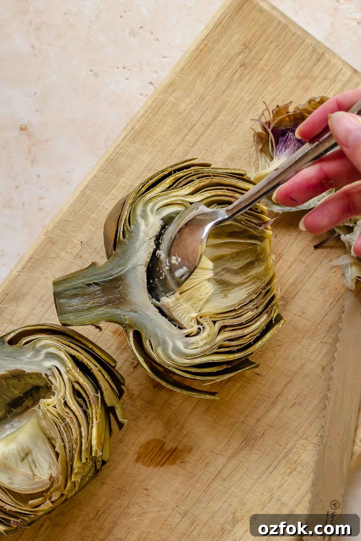 Grilled Marinated Artichokes with Lemon Aioli Recipe 10 A spoon removes the choke from half of a steamed artichoke.