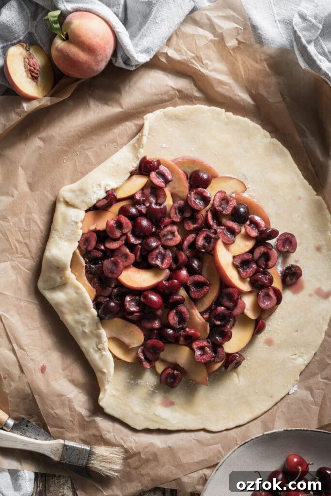 Peach and Cherry Galette Recipe with Flaky Golden Crust 3 Unbaked pie crust on parchment paper filled with sliced cherries and peaches.