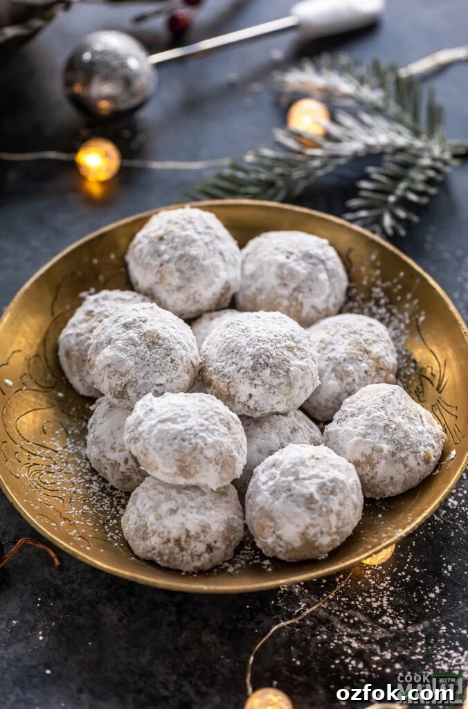Brown Butter Snowball Cookies Recipe — Buttery, Melt-in-Your-Mouth Treats 2 cookies coated in powdered sugar placed on a golden plate with lights in the background