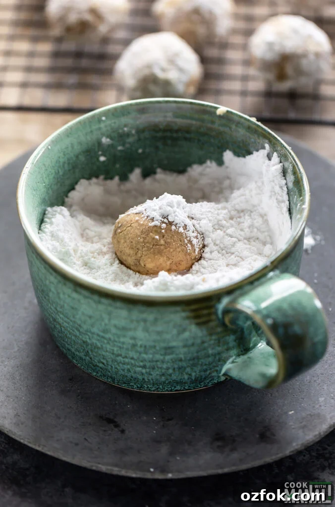 Brown Butter Snowball Cookies Recipe — Buttery, Melt-in-Your-Mouth Treats 5 a cookie being rolled in powdered sugar