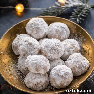 Brown Butter Snowball Cookies Recipe — Buttery, Melt-in-Your-Mouth Treats 7 cookies coated in powdered sugar placed on a golden plate with lights in the background