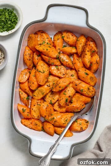 Air fryer carrots served in a white dish with fresh parsley and salt and pepper on the side.