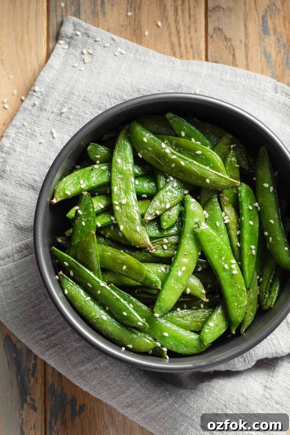 Crispy Air-Fried Snap Peas Recipe (15-Minute Side) 8 Roasted sugar snap peas in a black bowl on top of a grey napkin.