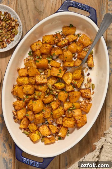 Air fryer butternut squash cubes in a serving dish with chopped pecans, pumpkin seeds and fresh herbs.