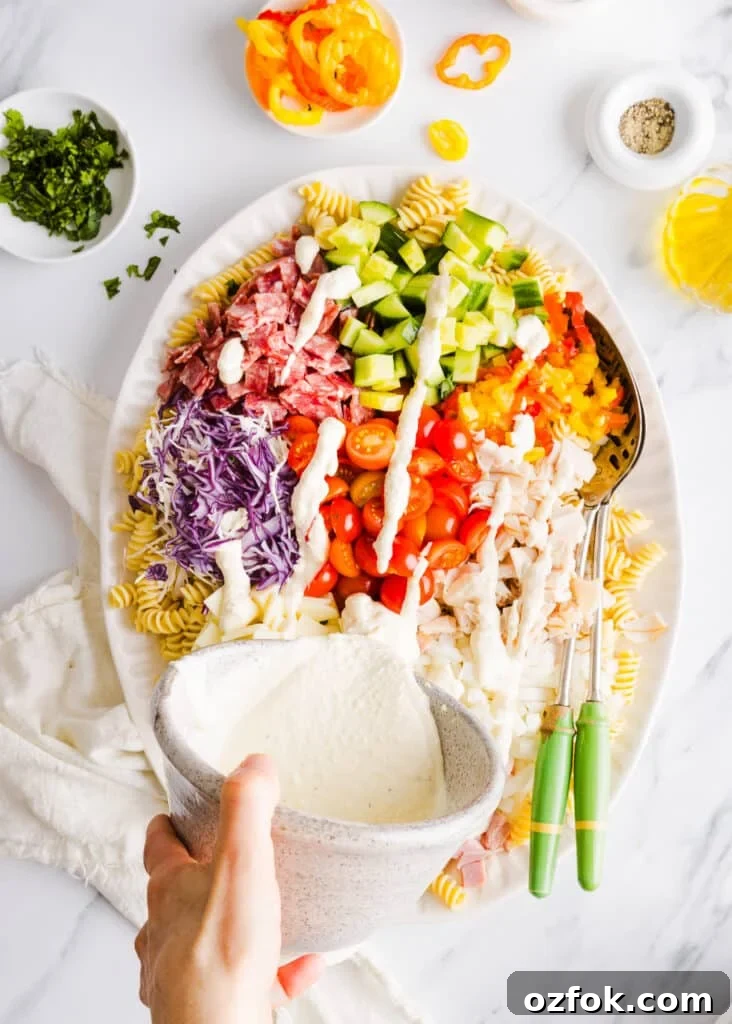 Grinder Pasta Salad Recipe with Italian Meats and Cheese 7 Grinder pasta salad dressing being poured onto a platter full of ingredients.