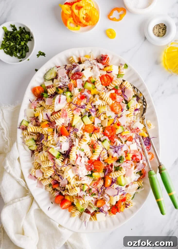 Grinder Pasta Salad Recipe with Italian Meats and Cheese 8 Grinder pasta salad on a large white platter with two serving spoons.