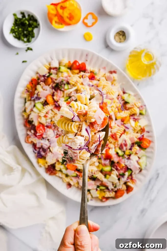 Grinder Pasta Salad Recipe with Italian Meats and Cheese 9 A spoonful of grinder pasta salad with a platter full of grinder pasta salad in the background.