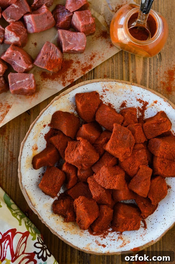 Chunks of raw sirloin steak coated with smoked paprika. Other uncoated steak sits next to it on butcher paper with a jar of smoked paprika. 