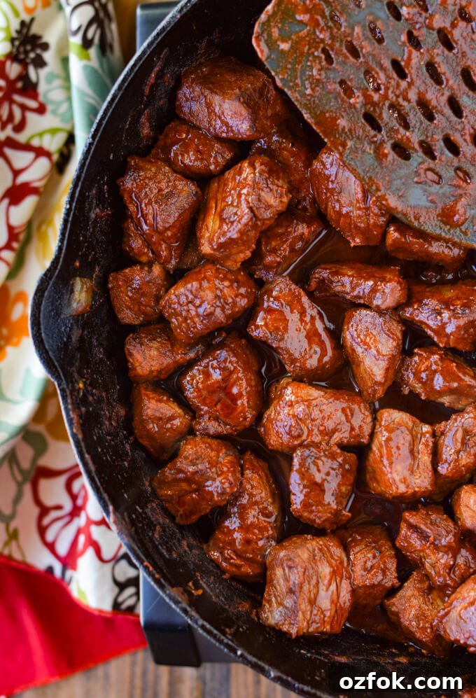 A cast iron skillet with cooked chunks of smoked paprika coated sirloin steaks next to a colorful napkin.
