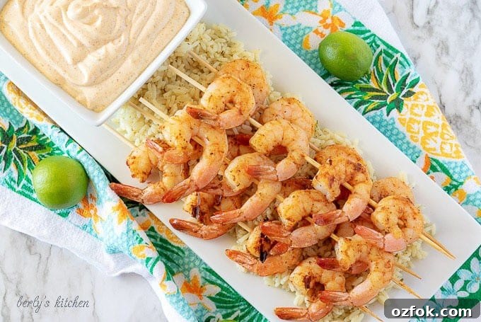 Key Lime Grilled Shrimp with Creamy Aioli Sauce 2 An aerial photo of grilled shrimp on skewers, served over rice on a white rectangular plate.