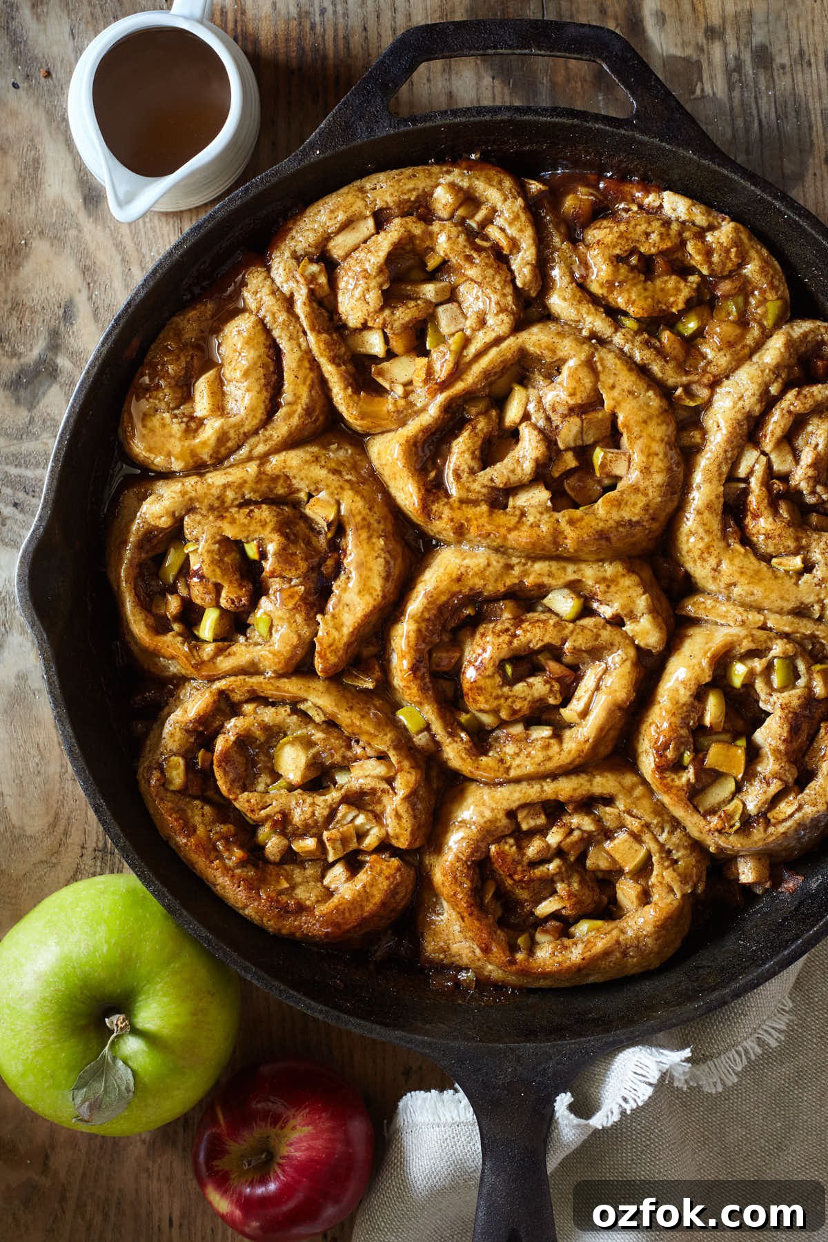 Caramel Apple Cinnamon Sticky Buns Recipe 6 Caramel apple cinnamon buns cooling on a wooden table in a cast iron pan
