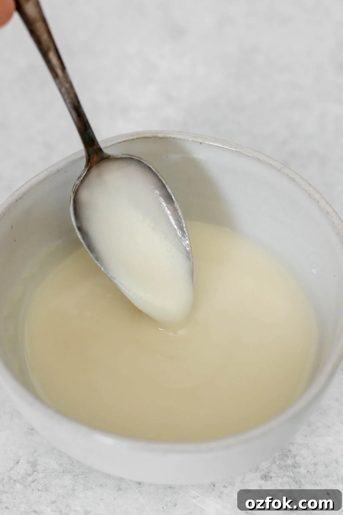 Paleo Coconut Butter Glaze Recipe for Cakes and Donuts 2 Coconut butter glaze dripping from a spoon in a small ceramic bowl.