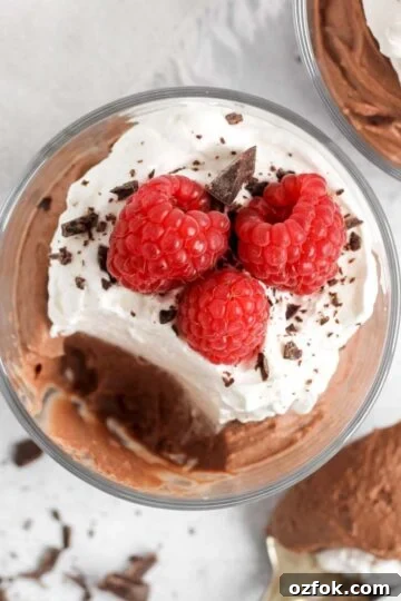 Chocolate mousse topped with whipped cream and raspberries in a small serving dish with a spoonful taken from the dish.