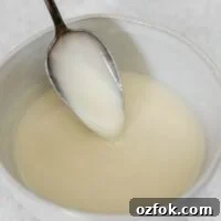 Paleo Coconut Butter Glaze Recipe for Cakes and Donuts 14 Coconut butter glaze dripping from a spoon in a small ceramic bowl.