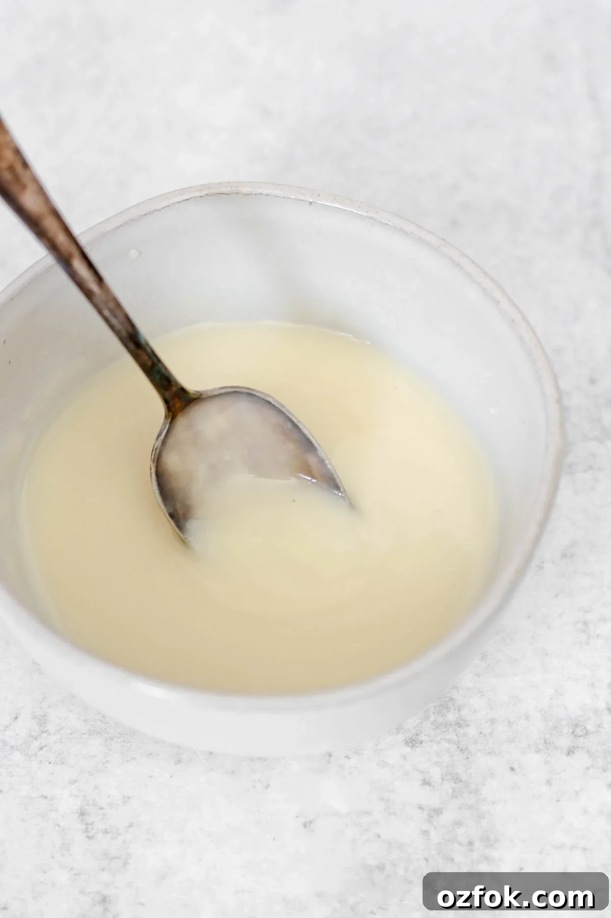 Paleo Coconut Butter Glaze Recipe for Cakes and Donuts 7 Coconut butter glaze in a bowl with a small spoon scooping up some glaze.