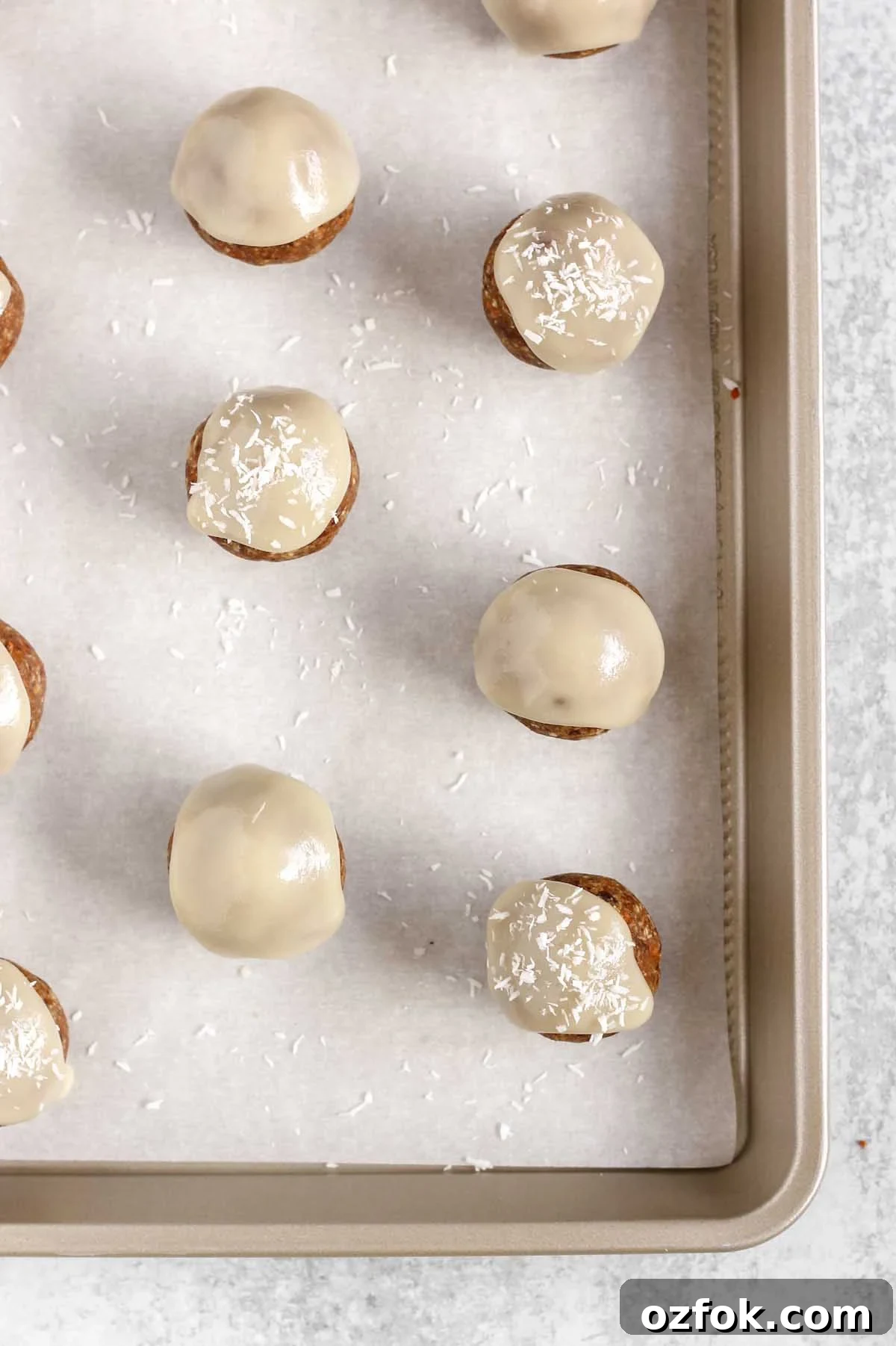 Paleo Coconut Butter Glaze Recipe for Cakes and Donuts 8 Carrot cake energy balls topped with glaze and sprinkled with coconut flakes on a cookie sheet.