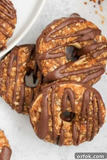 Three Samoa cookies slightly stacked on a gray surface with additional cookies around the side.