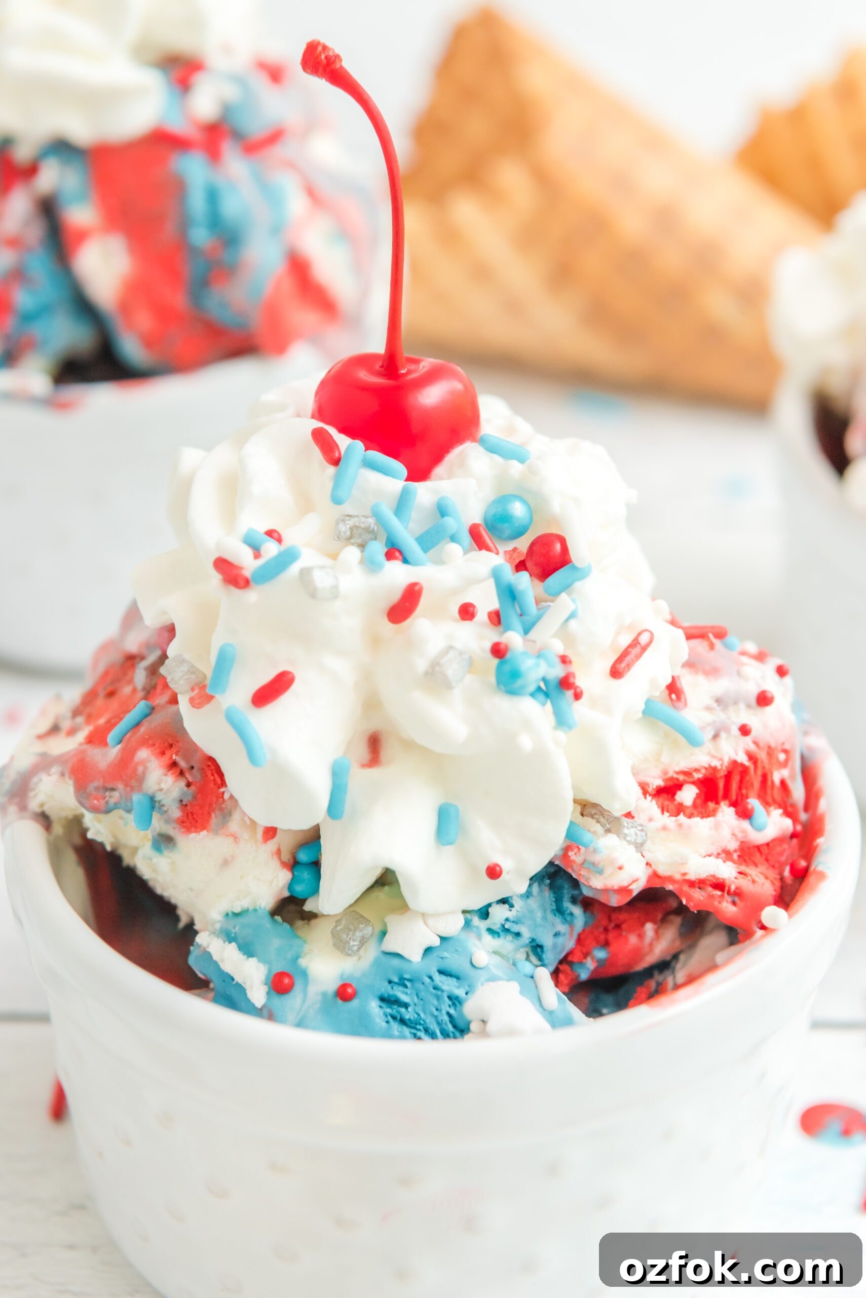 Patriotic Red, White & Blue Ice Cream Recipe for Summer Parties 2 Red, White & Blue Ice Cream in a white bowl topped with whipped cream and a cherry