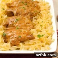 Classic Hungarian Chicken Paprikash Recipe — Authentic Paprikas 3 Easy Chicken Paprikas served over a bed of buttered egg noodles, garnished with chopped parsley on a rectangular white platter.
