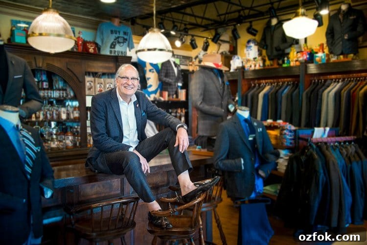 Bruce Julian sitting on a bar with feet on bar stools surrounded by men's clothes.