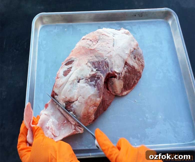 Grilled Australian Leg of Lamb Roast Recipe 3 trimming lamb roast on pan while wearing orang gloves