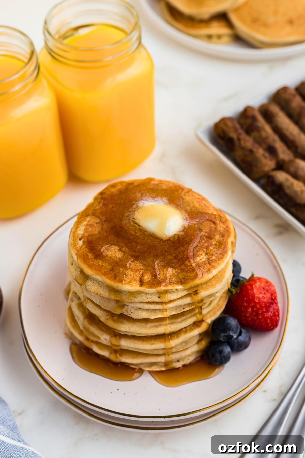 Light and fluffy golden pancakes stacked on a white plate with berries and syrup. 