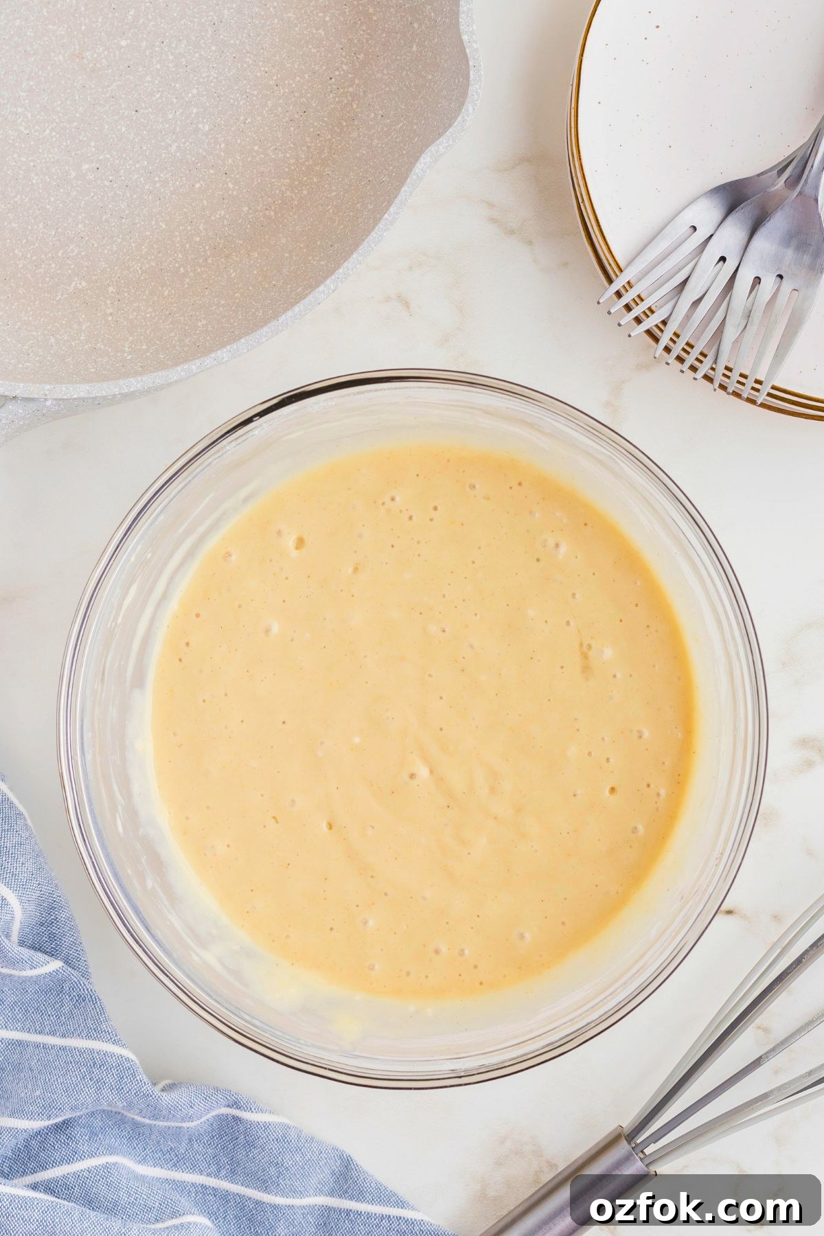 Gluten free pancake batter in a large clear glass bowl in front of the skillet. 