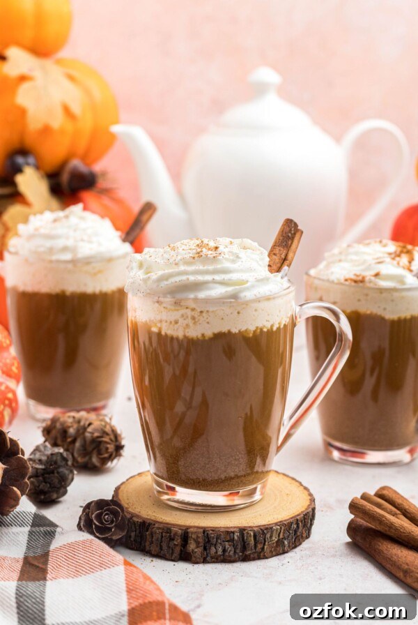 Cups of coffee topped with whipped cream, in front of white pot, on a marble board.