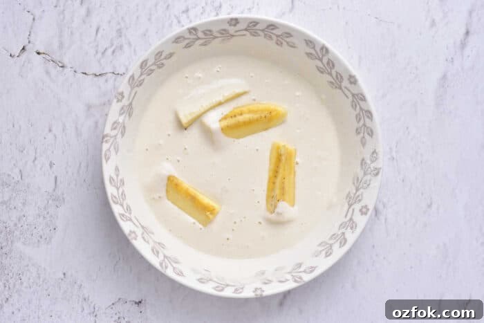 A bowl of tempura is adorned with banana slices, reminiscent of delicate banana tempura, set against a white, textured background.