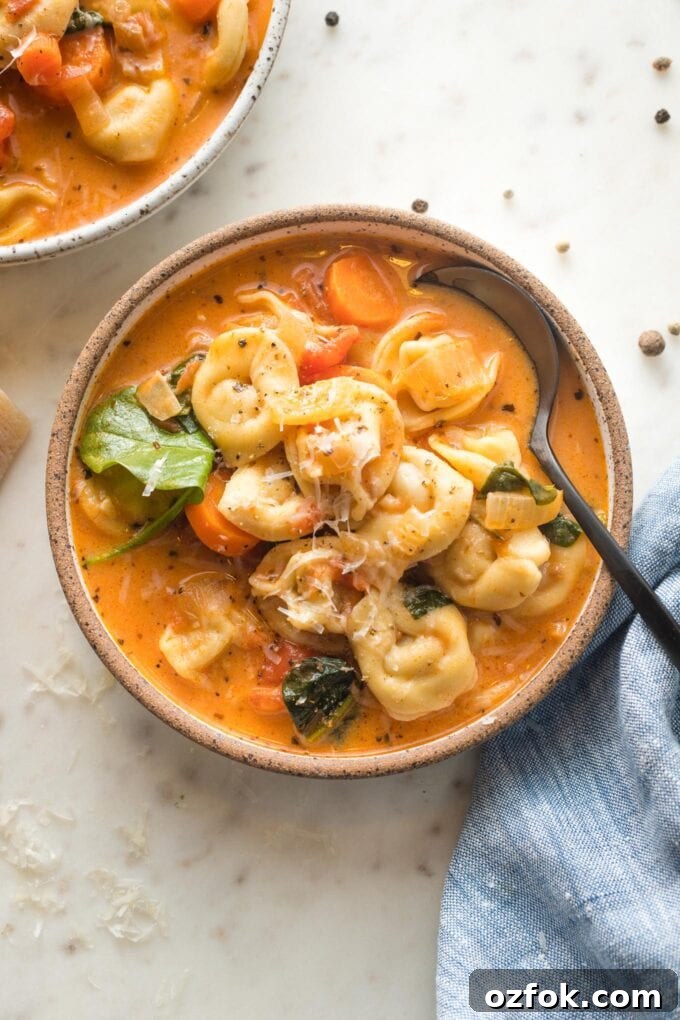 Small bowl of creamy tomato tortellini soup served with black pepper and fresh grated Parmesan.