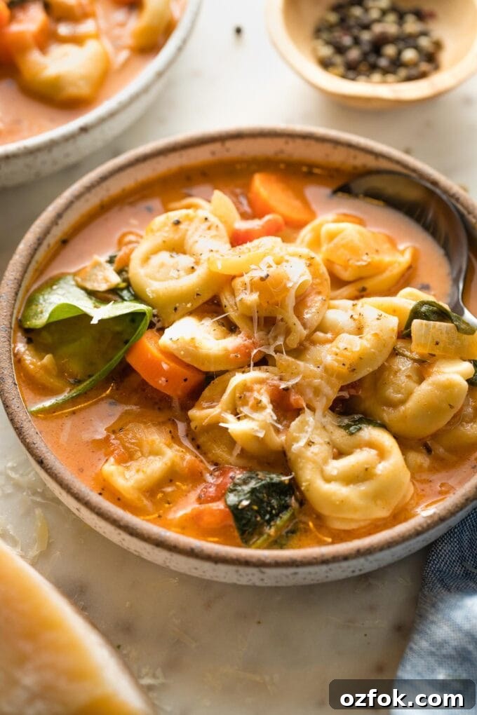 Side view of a spoon lifting a bite of creamy tomato tortellini soup.
