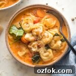 Small bowl of creamy tomato tortellini soup served with black pepper and fresh grated Parmesan.