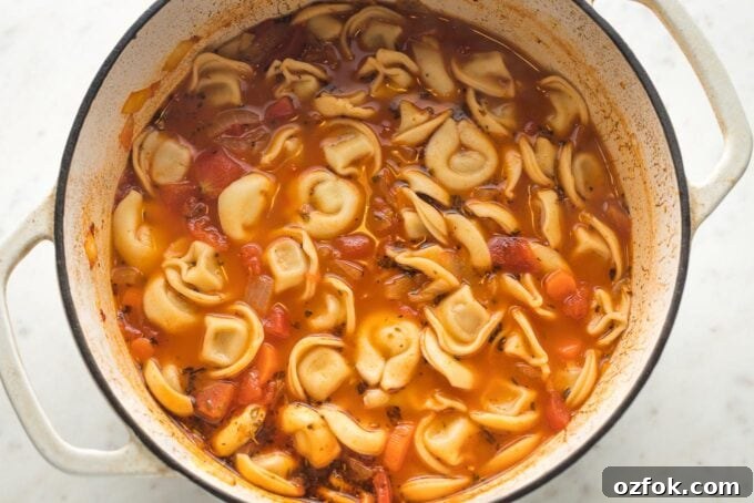 Broth bubbling with tortellini cooking inside of Dutch oven.