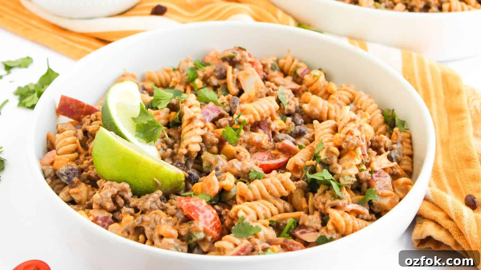 29 Irresistible Salad Recipes Everyone Will Love 12 A bowl of fusilli pasta mixed with ground beef, black beans, chopped tomatoes, and herbs, garnished with lime wedges.