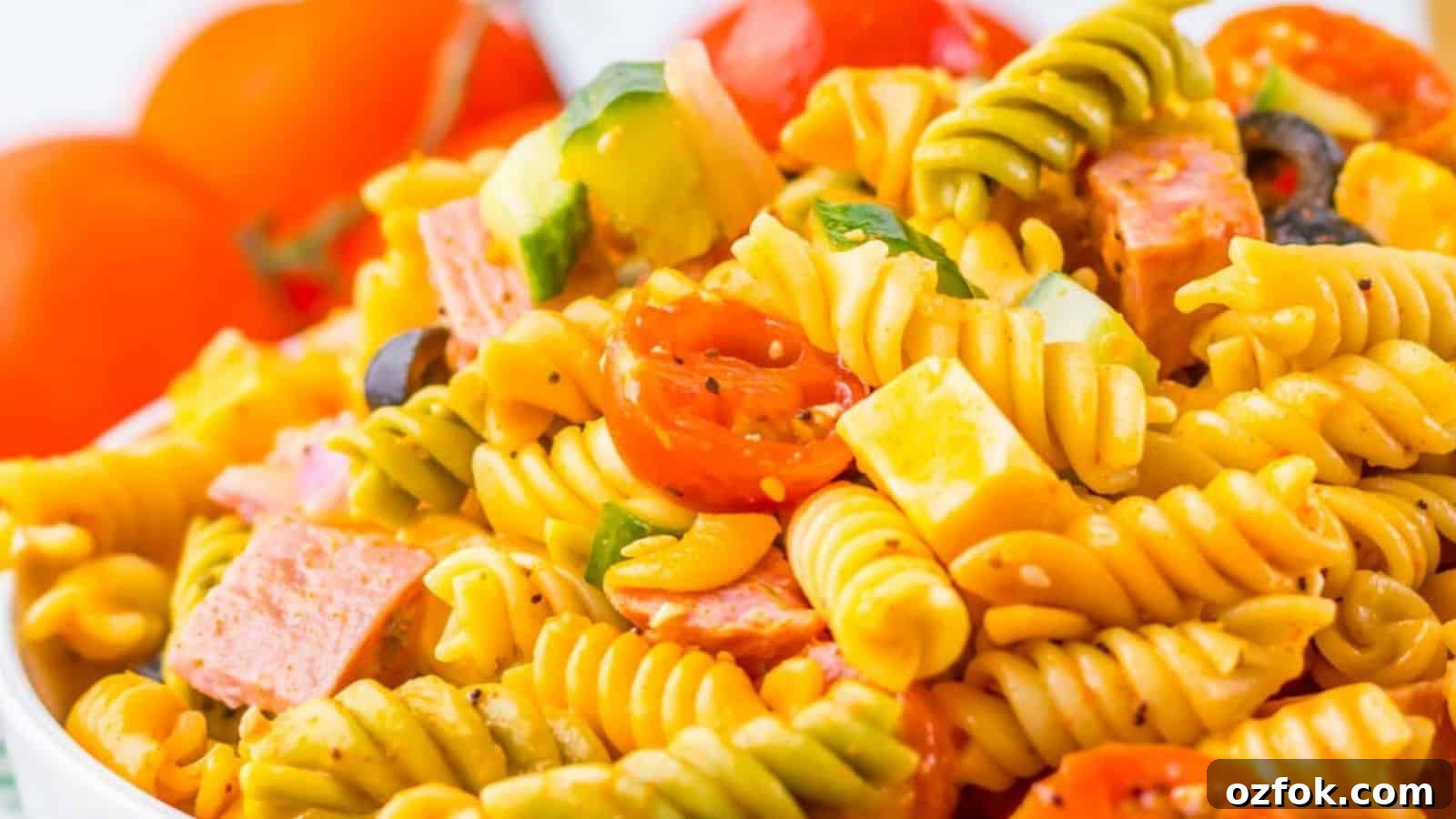 29 Irresistible Salad Recipes Everyone Will Love 15 A vibrant pasta salad with fusilli, cherry tomatoes, bell peppers, black olives, and diced salami in a clear bowl.