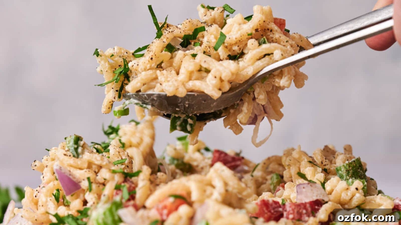 29 Irresistible Salad Recipes Everyone Will Love 16 A spoon lifting a serving of creamy macaroni salad with diced red onion and fresh herbs, with pepper sprinkled on top.
