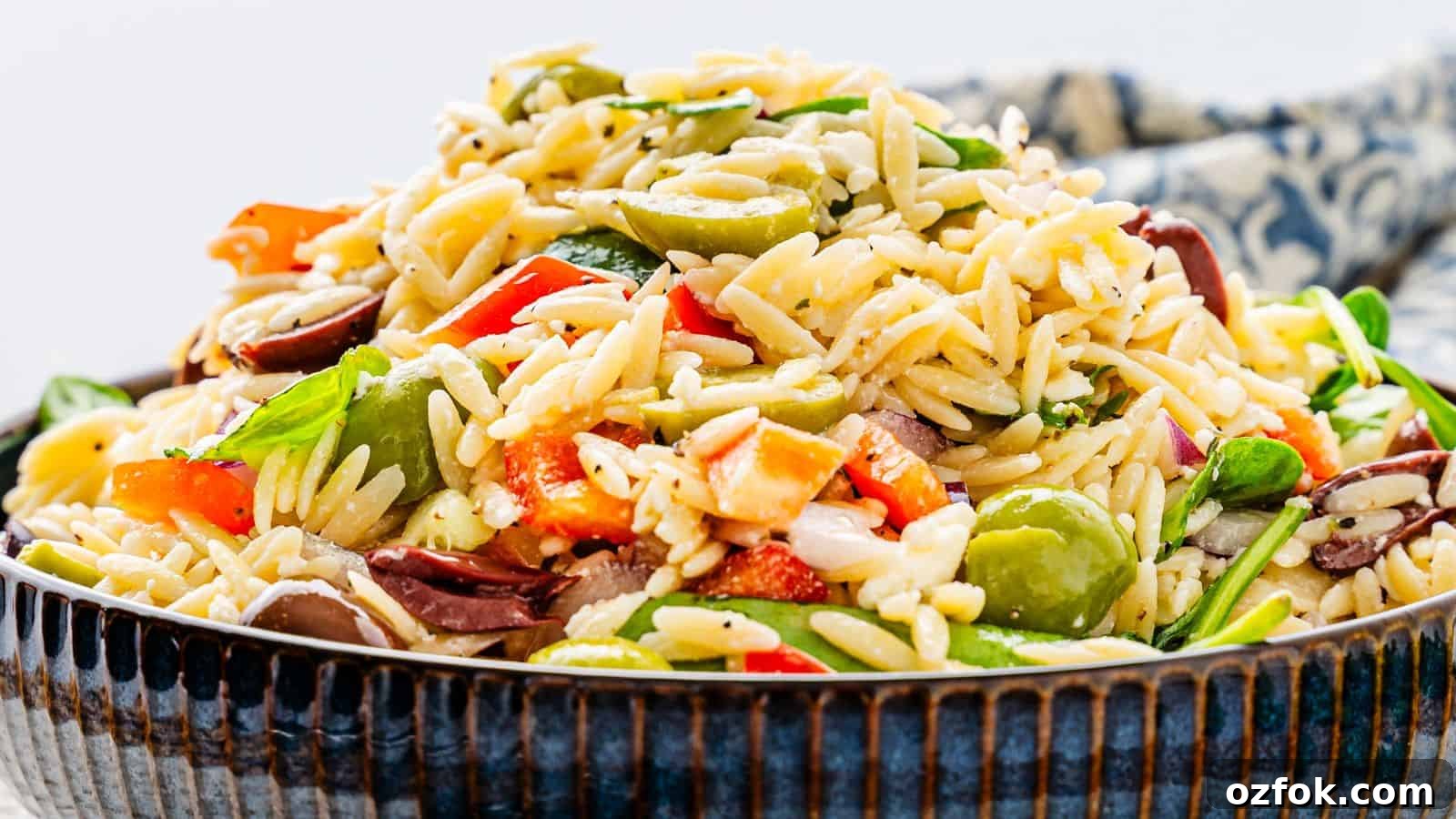 29 Irresistible Salad Recipes Everyone Will Love 19 A bowl of orzo salad with mixed vegetables, including olives, tomatoes, and spinach, garnished with herbs.