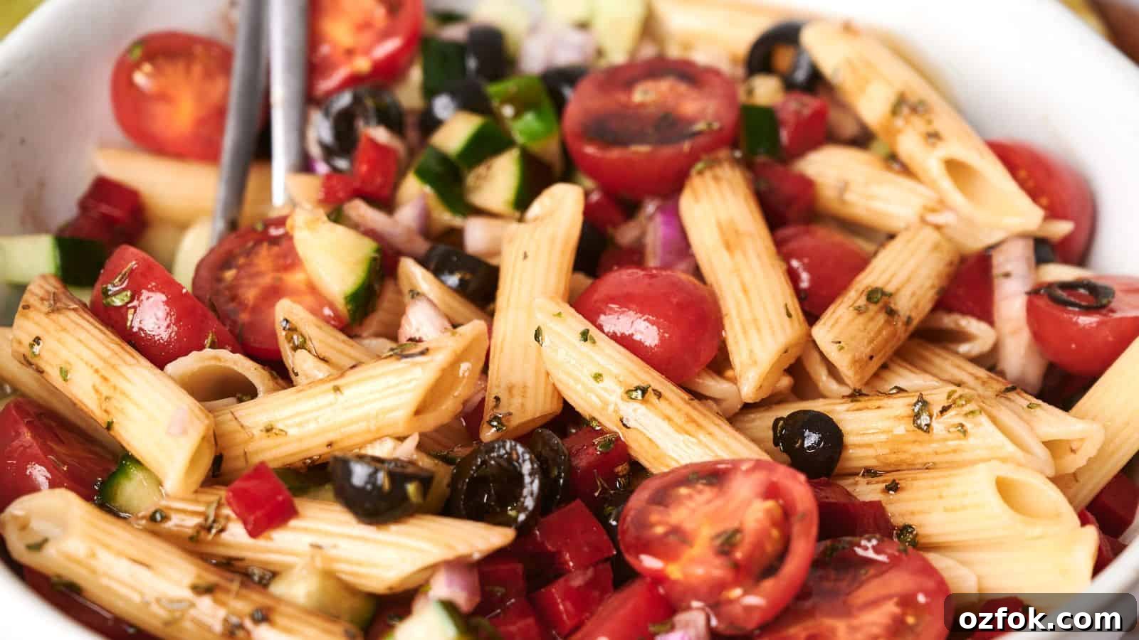 29 Irresistible Salad Recipes Everyone Will Love 24 A bowl of vibrant pasta salad with penne, cherry tomatoes, black olives, diced cucumbers, red onions, and a drizzle of dressing.