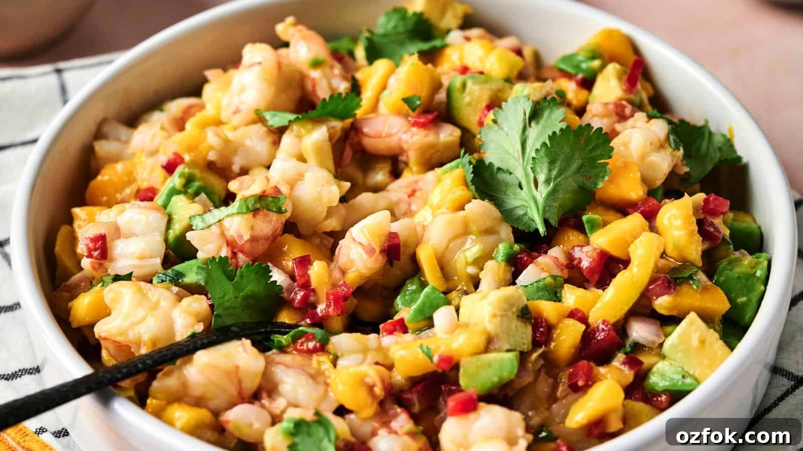 29 Irresistible Salad Recipes Everyone Will Love 25 A bowl of shrimp ceviche with diced mango, avocado, red onion, red pepper, and cilantro, with a spoon inside.