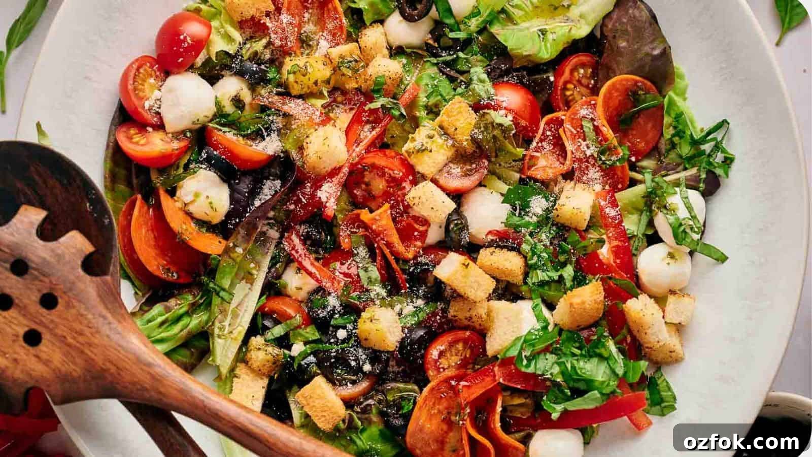 29 Irresistible Salad Recipes Everyone Will Love 27 Homemade pizza salad in a serving bowl with wooden salad servers resting on top.