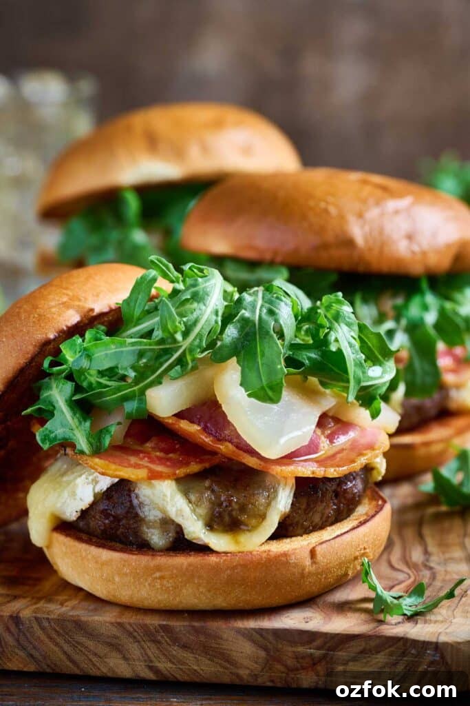 Brie Burger with Bourbon-Poached Pears and Crispy Pancetta 2 hamburgers topped with brie cheese, crisp pancetta and fresh arugula on a wooden board